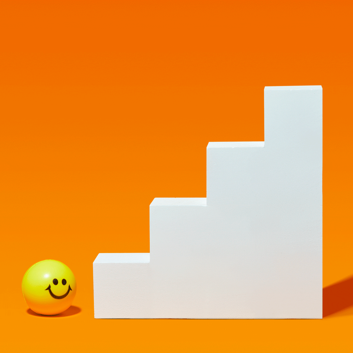 yellow smiley face ball bouncing up white staircase against an orange background