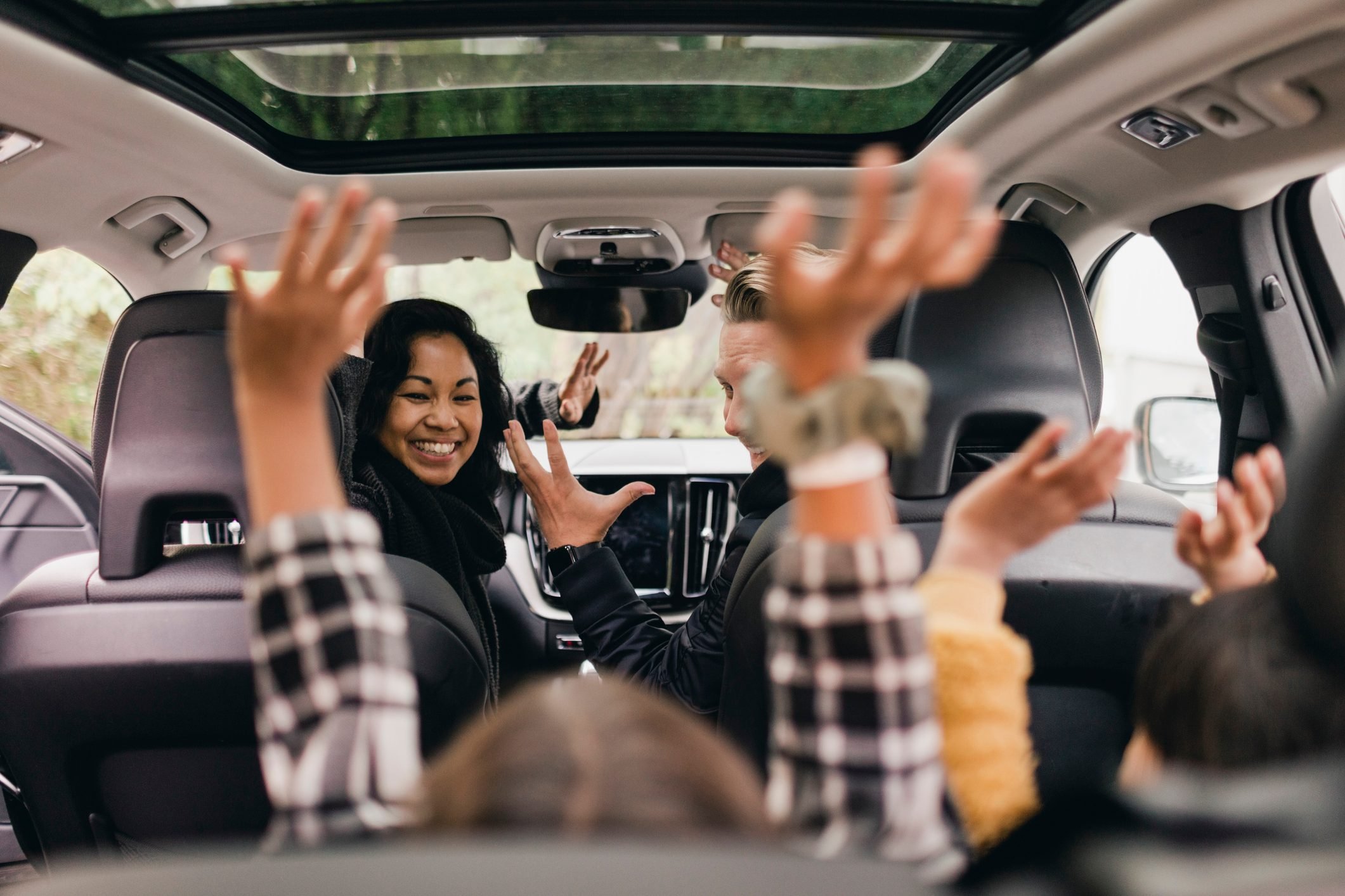 Cheerful family raising hands while enjoying road trip in electric car