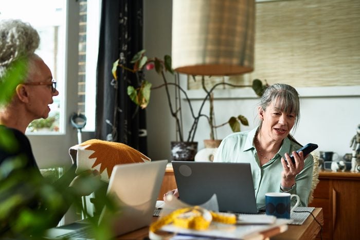 Mature female entrepreneur speaking into smart phone at home