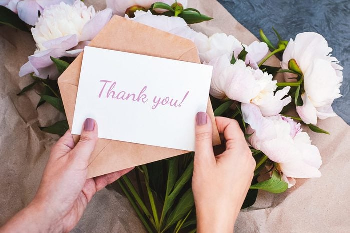 Thank you card in hands, message, envelope, pink peony flowers bouquet