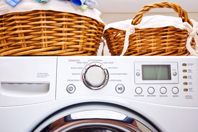 close up of buttons on a front load washing machine with baskets of laundry sitting on top